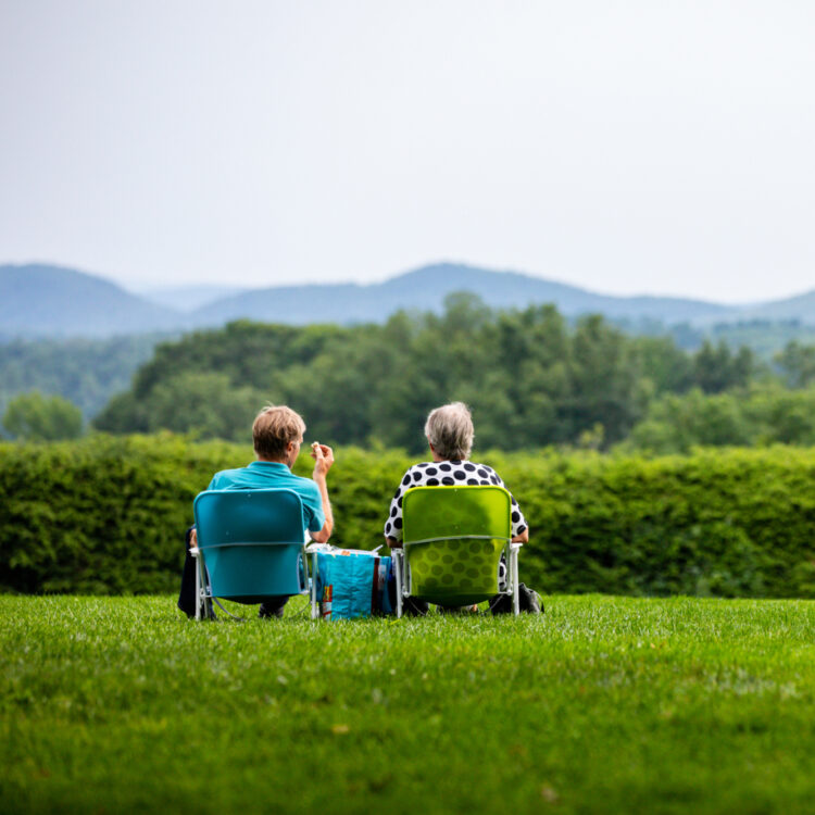 Two people sit in lawn chairs on Tanglewood lawn looking out at nature surrounding them